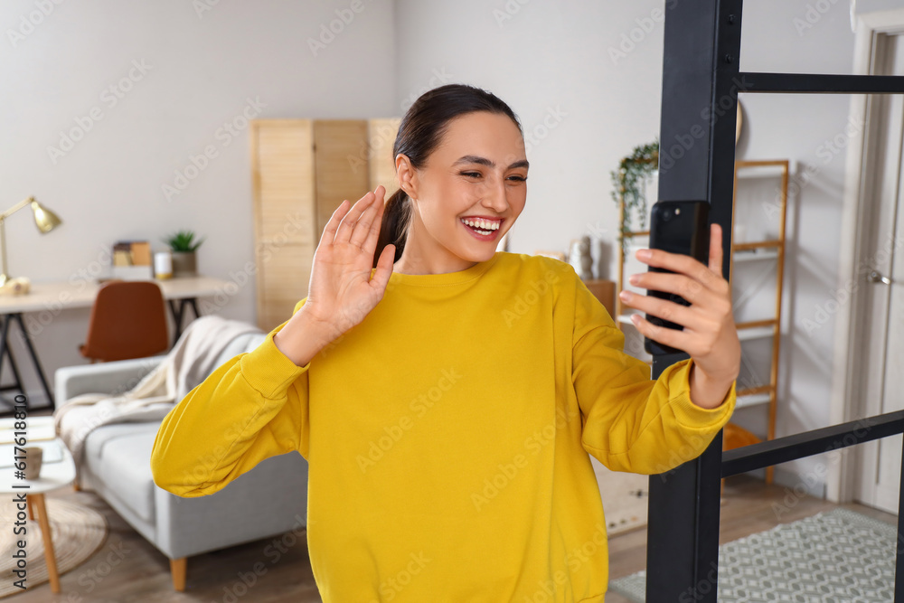 Happy young woman with mobile phone video chatting at home