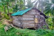 A thatched house with a corrugated metal roof built on the edge of a hill in rural Oriental Mindoro Province, Philippines. A wooden water buffalo sled is on the grass.
