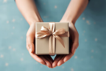 Wall Mural - woman's hands hold brown present wrapping gift box with bright gold ribbon and bow