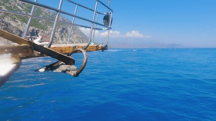 Wall Mural - A side view of the bow of the boat and the anchor. The boat sails through the blue calm sea. Beautiful mountains to the left and ahead. A boat ride around the amazing bays of the Mediterranean Sea