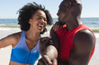 © wavebreak3 - Happy, fit african american couple exercising, stretching and smiling on sunny beach