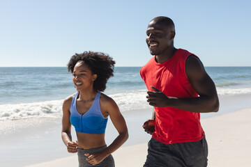 Happy, fit african american couple exercising, running on sunny beach