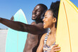 © wavebreak3 - Happy african american couple holding surfboards standing on sunny beach talking