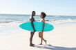 © wavebreak3 - Happy african american couple holding surfboard smiling at each other standing on sunny beach