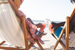 © wavebreak3 - Happy african american couple sitting in deckchairs making a toast with bottles on sunny beach