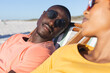 © wavebreak3 - Happy african american couple in sunglasses sitting in deckchairs relaxing on sunny beach