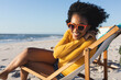 © wavebreak3 - Portrait of happy african american woman sitting in deckchair and smiling on sunny beach