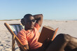 © wavebreak3 - Happy african american man in sunglasses sitting in deckchair reading book on sunny beach