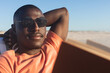 © wavebreak3 - Happy african american man in sunglasses sitting in deckchair reading book on sunny beach