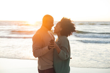 Happy african american couple dancing and smiling on sunny beach