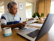© WavebreakMediaMicro - Senior biracial man doing paperwork and using laptop in dining room