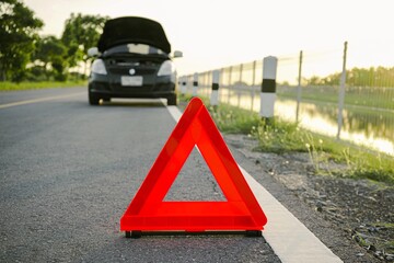 Wall Mural - Close-up of a red emergency stop sign on a background of a broken black car on the road. Red emergency stop sign with broken down car on the road waiting to be repaired.