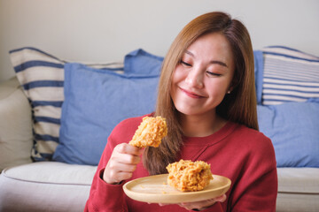 Wall Mural - Portrait image of a young woman holding and eating fried chicken at home