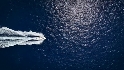 Wall Mural - high aerial top view of a motor yacht cruising with speed over blue, sparkling ocean and leaving a t