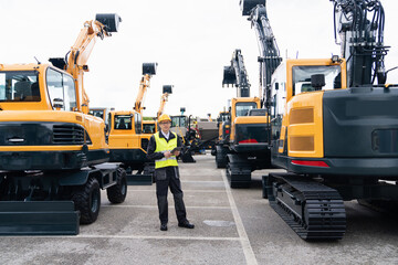 Aufkleber - Engineer in a helmet with a digital tablet stands next to construction excavators.