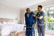 Happy diverse male doctor helping senior male patient using crutches at home