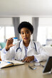 © wavebreak3 - African american female doctor holding medication making video call in bright room