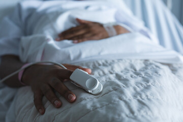 Wall Mural - Midsection of african american female patient with pulse oximeter on hand, lying on bed at hospital