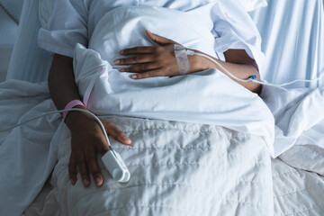 Wall Mural - Midsection of african american female patient with drip on hand, lying on bed in hospital room