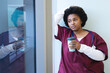Thoughtful african american female doctor wearing scrubs, holding coffee and looking through window