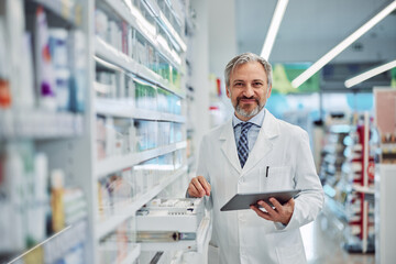 Portrait of a grey-bearded male pharmacist using a digital tablet for work.