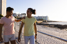 Happy Biracial Gay Male Couple Walking On Promenade By The Sea, Copy Space
