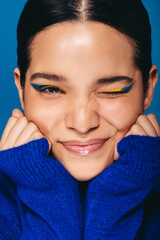 Wall Mural - Wearing vibrant eye makeup, woman winks at the camera in a studio