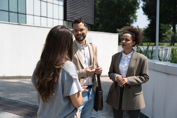 Wall Mural - Group of coworkers walking outside in front of office buildings discuss about business plan. Businesspeople marketing sale experts talking ideas and marketing tactics