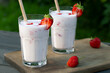 Strawberry smoothie in two glass glasses and fresh strawberries on a wooden table in the yard