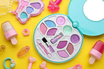 eye shadow palette and other decorative cosmetics for kids on yellow background, flat lay