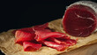 Whole and sliced bresaola on paper on a cutting board