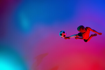 Wall Mural - Aerial view of playing little boy during training with football ball in gradient red-blue neon light. Concept of action, sportive lifestyle, team game, health, energy