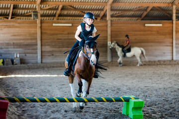 Wall Mural - Pretty young girl doing equestrian show jumping on her pony in a farm