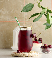 Wall Mural - Cherry juice in a transparent glass and fresh cherries on a white table