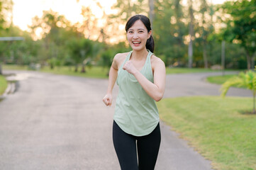 Wall Mural - Fit Asian young woman jogging in park smiling happy running and enjoying a healthy outdoor lifestyle. Female jogger. Fitness runner girl in public park. healthy lifestyle and wellness being concept