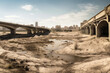 © ADDICTIVE STOCK - Generative AI illustration of dried river with puddles of water bottom in post apocalyptic city with damaged buildings