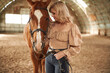 Sunny day. Standing with animal. Beautiful young woman is with horse indoors