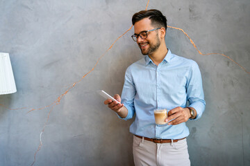 Wall Mural - Portrait of a smiling young business man using smartphone and holding cup of coffee