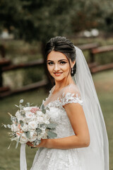 Wall Mural - Portrait of a brunette bride in a white wedding dress with a wedding bouquet in the park. Full length photo. White lace wedding dress