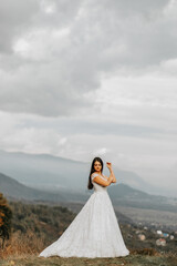 Wall Mural - Beautiful bride against the background of autumn mountains in front. A luxurious white dress. Wedding ceremony on top of the mountain. Free space.