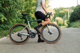 Fototapeta Uliczki - Photo of a male professional cyclist with a road bike outside the city on an asphalt road.