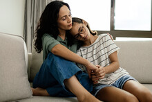 Caring Mother Comforting Her Teenage Daughter, Both Sitting On The Couch At Home, Sharing A Tender And Supportive Moment