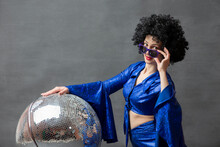 Girl With A Disco Ball In An Afro Wig On A Gray Background. Disco Style From The Seventies Or Eighties.