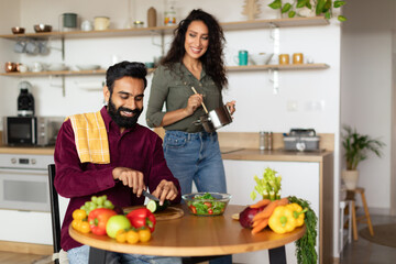 Happy middle eastern couple cooking together, making delicious meal, man preparing vegetable salad, kitchen interior