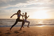 Happy young slim european women twins in sportswear run at morning, freeze in air at sea beach, outdoor