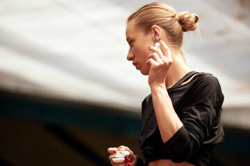 Wall Mural - A cute young fitness girl takes out wireless headphones from a case and puts them in the ears. Attractive blonde in a black t-shirt listens to music and prepares for a workout. Active lifestyle.