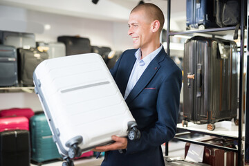 Wall Mural - Positive confident man standing in a bag store carefully examines a travel suitcase