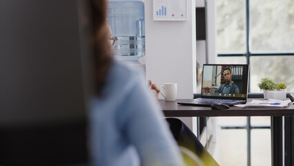 Wall Mural - Young person attending business meeting videocall in startup coworking space, using online teleconference chat. Female assistant talking to people on remote video conference, telework research.