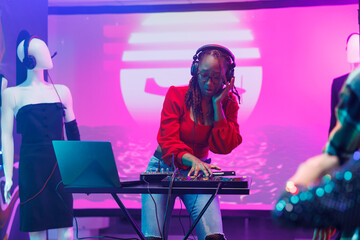 Woman dj in headphones mixing sound with controller while performing on stage with spotlights in nightclub. African american musician using digital music mixer during show in club