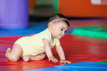 Wall Mural - Beautiful ten months baby girl crawling on a colorful background. Early stimulation for toddlers concept.